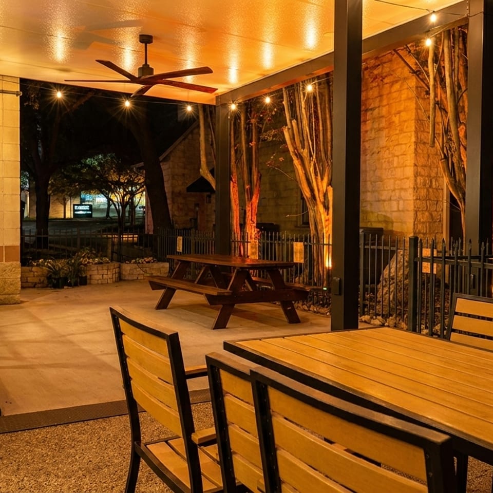 An outdoor patio at night with string lights, a ceiling fan, and wooden tables.